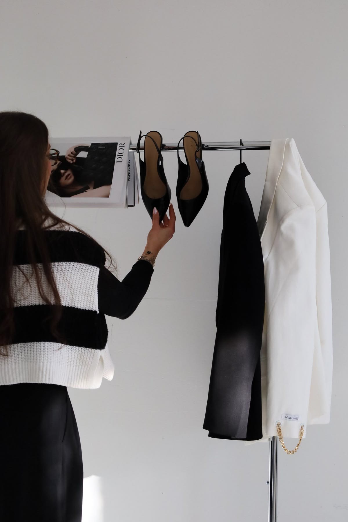 Mujer seleccionando tacones y blazer en un rack de ropa con luz natural